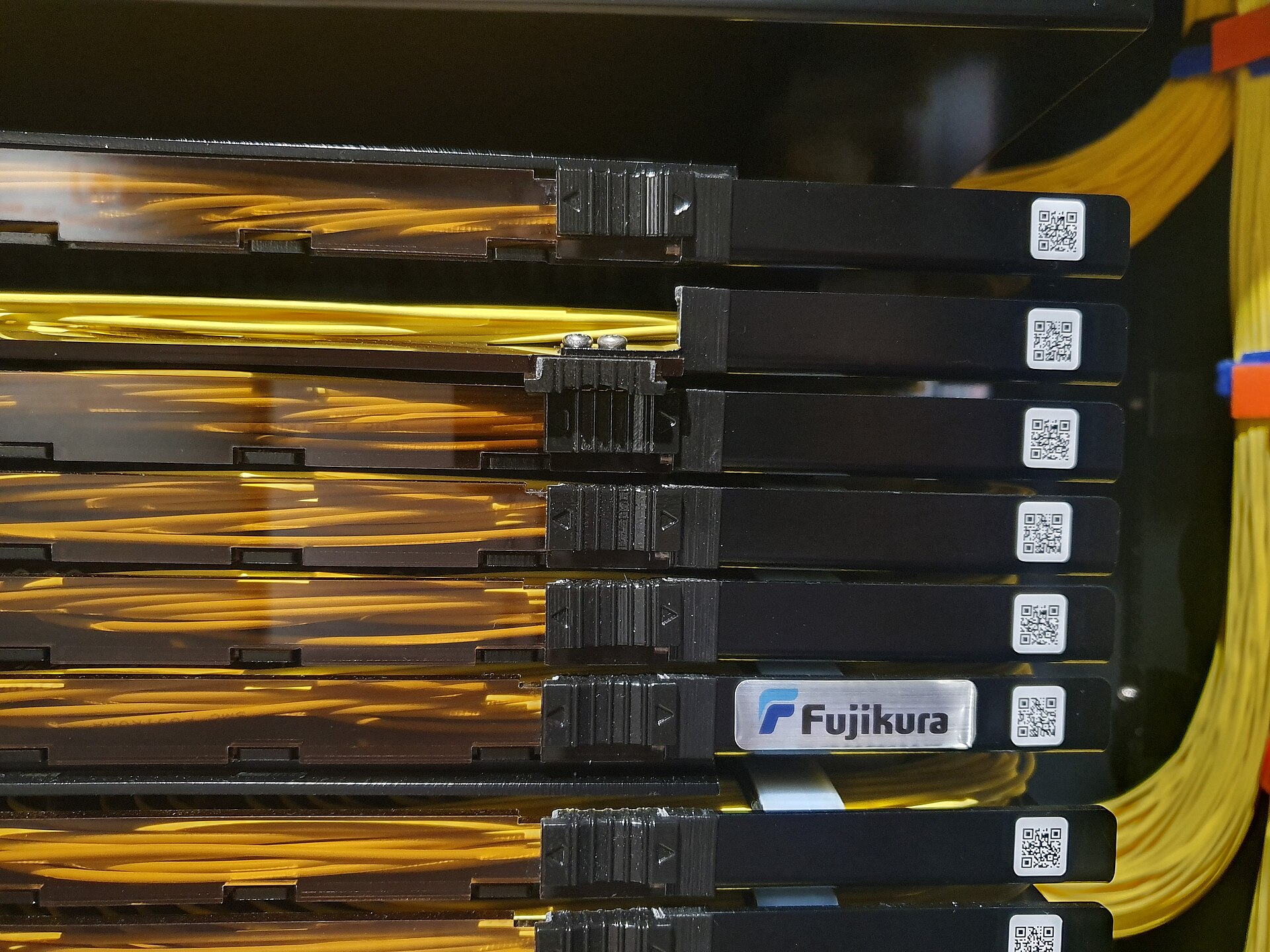 Stacked fibre splice trays with yellow optical fibre coiled inside and running down the side of the rack.